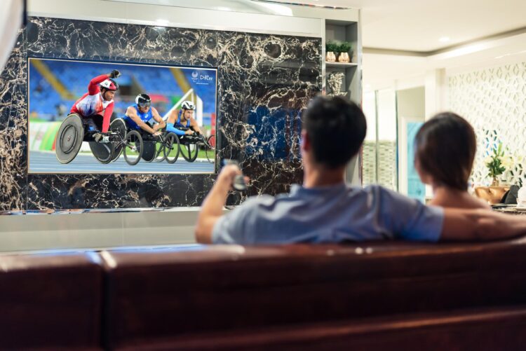 Asian couples watching white blank screen display television for advertising template background. People lifestyles concept. Lockdown social distancing work from home. Selective focus on TV